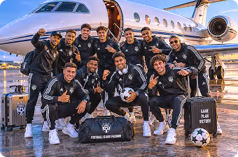 Smiling soccer team posing with gear in front of private jet at sunset on wet tarmac.