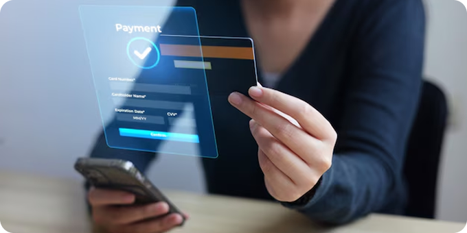 Person holding a credit card and a smartphone with a translucent digital payment confirmation interface showing card number, cardholder name, expiration date, CVV, and a checkmark for successful payment.