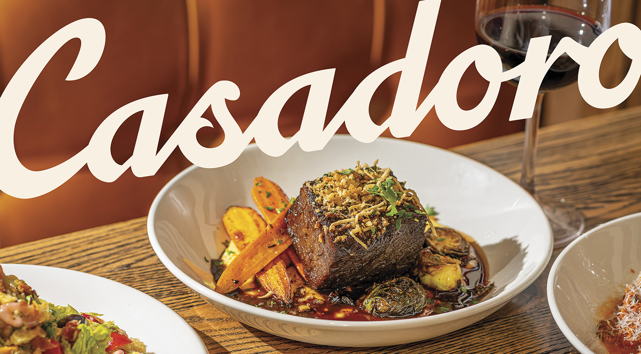 A stylized product shot featuring two ruby-red cocktails on a wooden board, garnished with lime wedges and fresh mint. The Casadoro logo is overlaid in a flowing script typeface, creating a sense of elegance and sophistication. The composition is complemented by strategically placed citrus fruit, adding pops of color and texture.