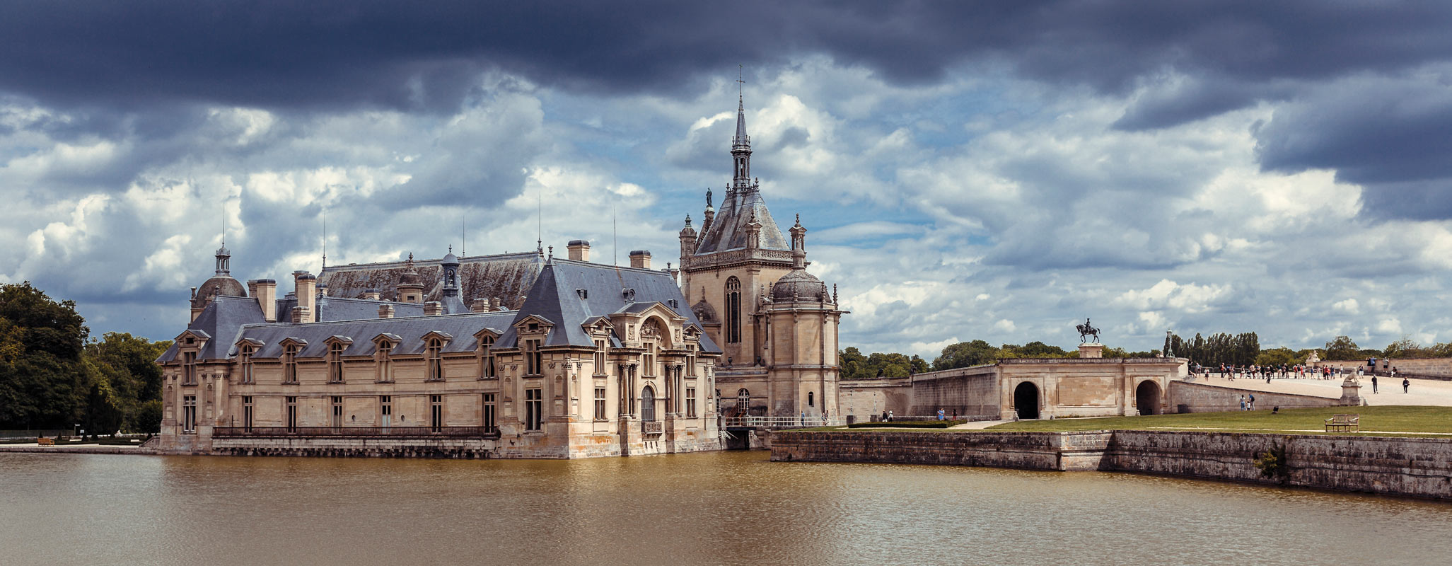Historic castle with ornate architecture surrounded by moat under a cloudy sky.