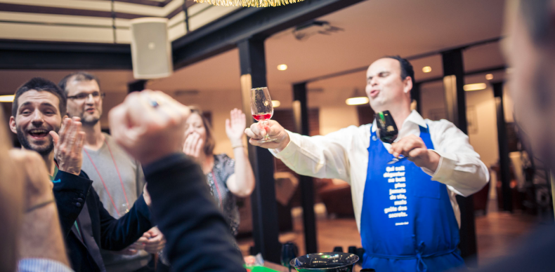 Person pouring red wine through a funnel into a wine bottle on a table with glasses and bottles in the background.