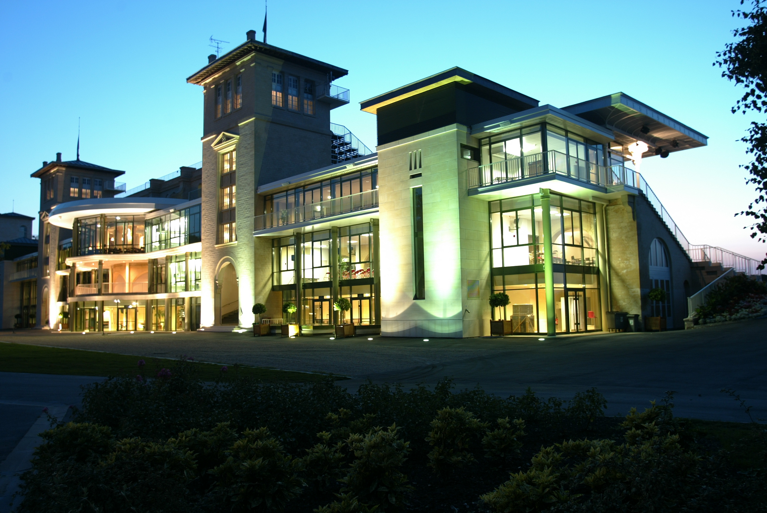 Illuminated modern building with large windows and towers at dusk with clear blue sky.