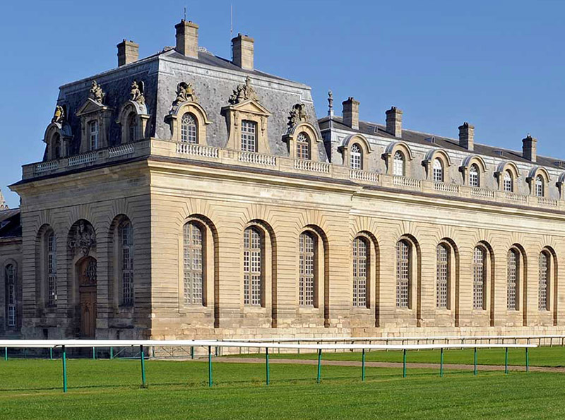 Historic stone building with large arched windows and ornate rooftop against a clear blue sky.