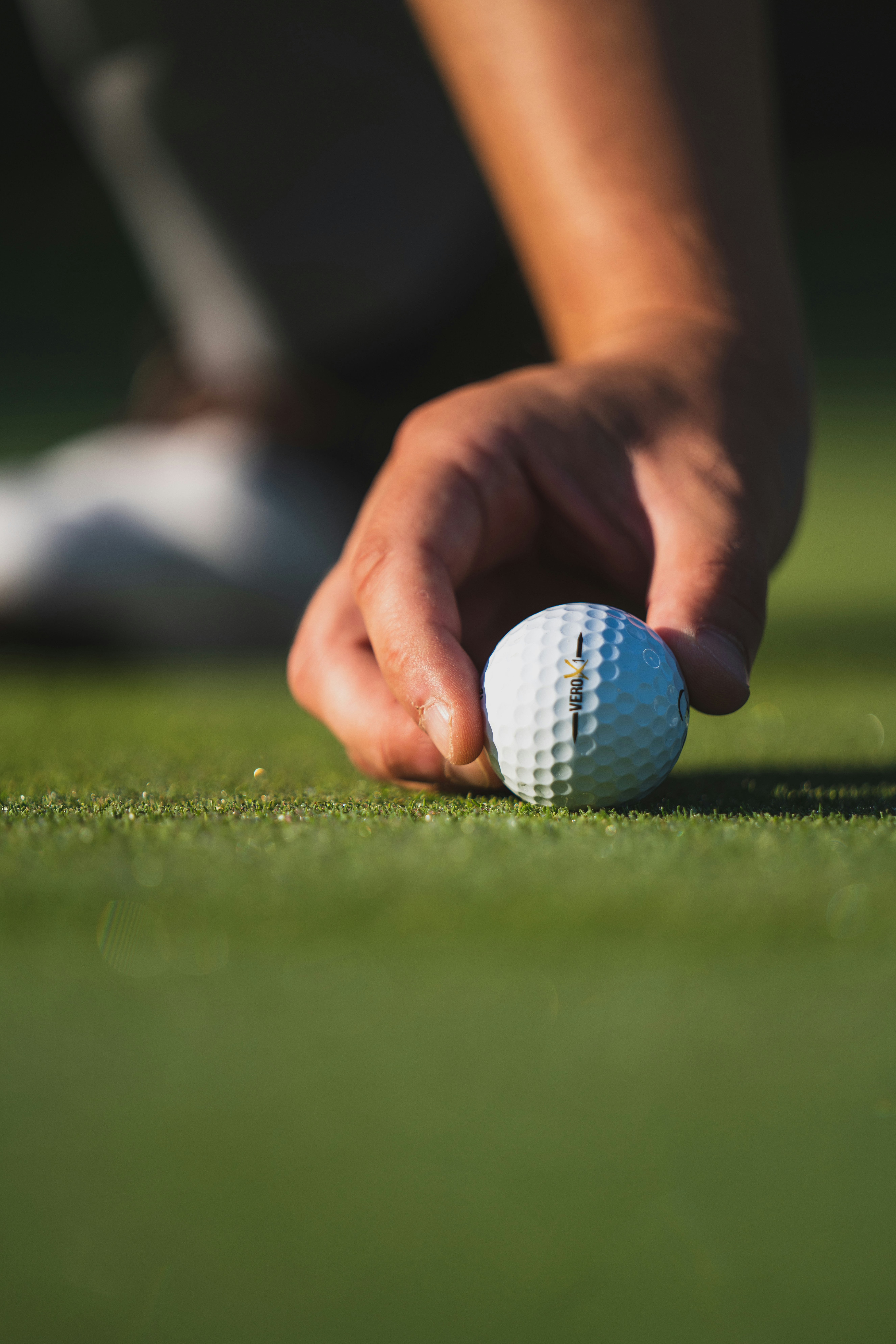 Hand placing a white golf ball on green grass with blurred background.