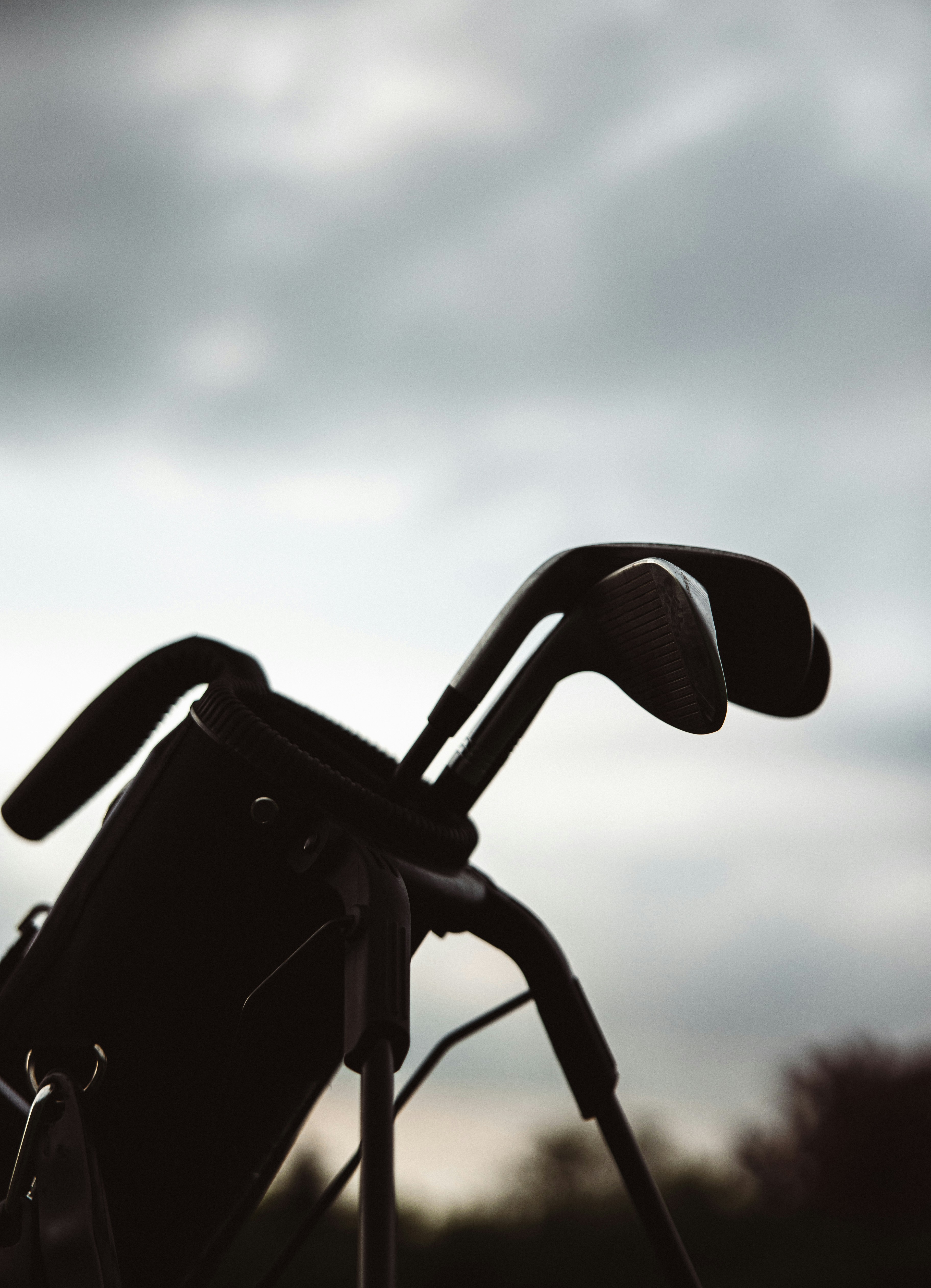 Silhouette of golf clubs in a golf bag against a cloudy sky at dusk.