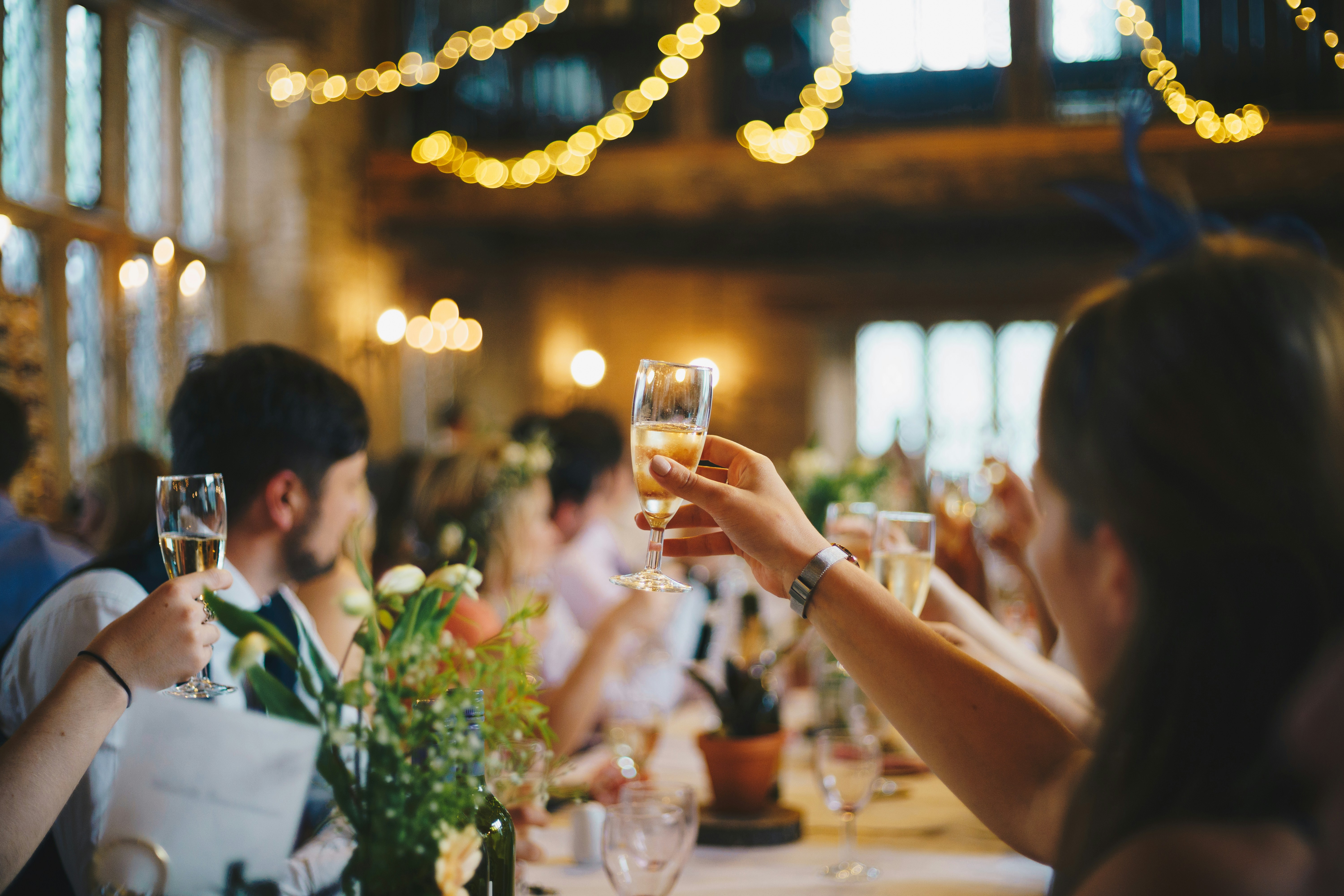People raising champagne glasses for a toast at a warmly lit, festive indoor gathering.