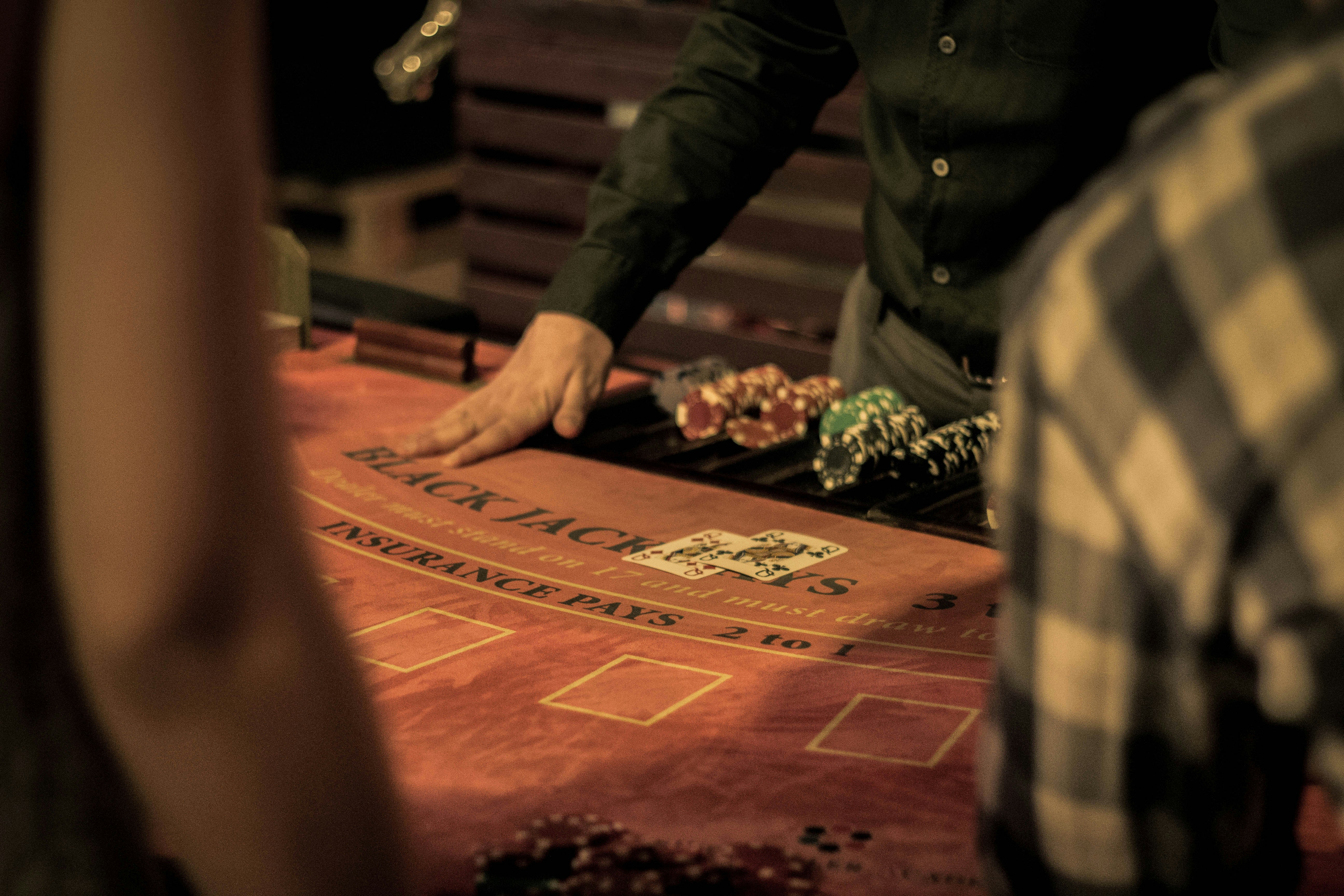 Casino dealer showing two playing cards on a blackjack table with poker chips stacked nearby.