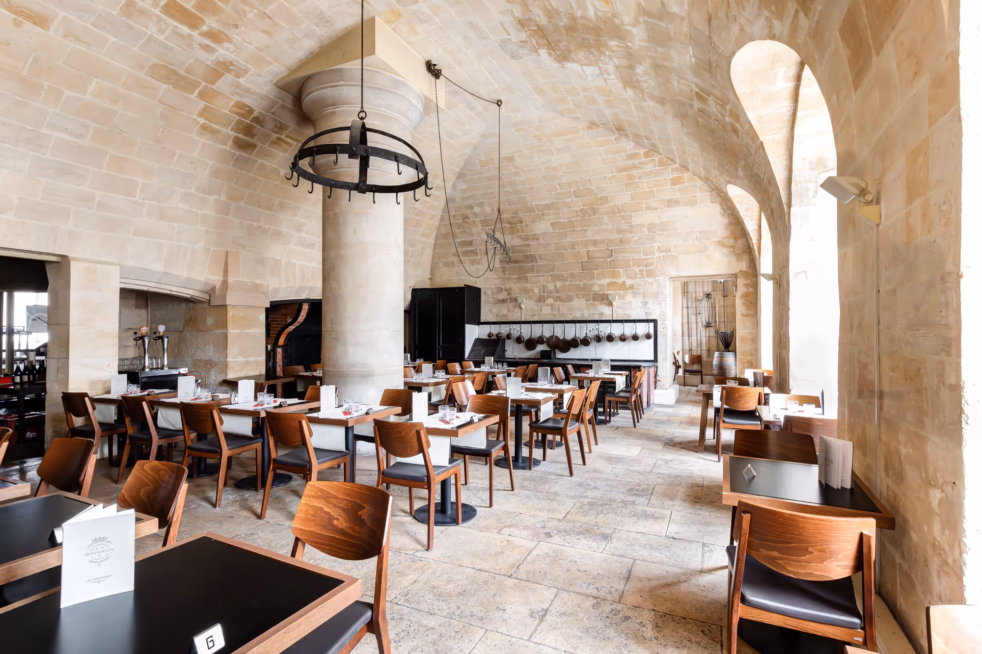 Bright dining area in a historic stone room with vaulted ceilings, wooden chairs, and tables set for service.