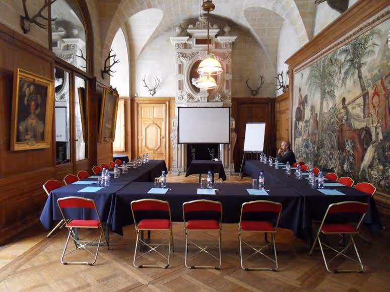 Elegant seminar room with U-shaped table setup, red chairs, wooden paneling, mounted deer antlers, and large tapestry on the wall.