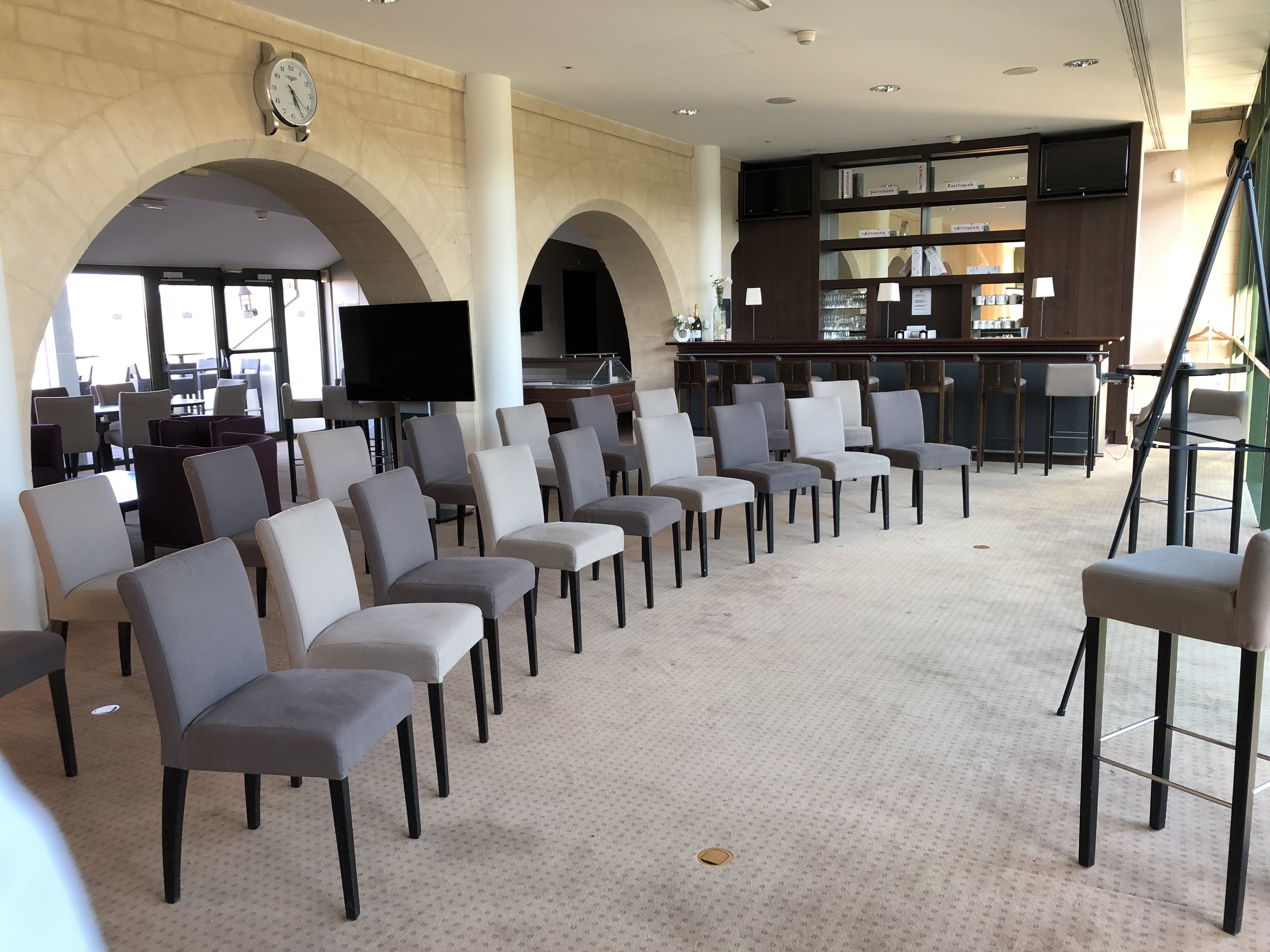 Conference room with rows of beige and gray chairs facing a whiteboard on a stand near a bar area with stools.