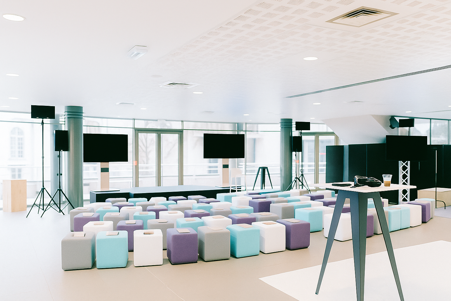 Bright modern seminar room with rows of colorful cube seats facing multiple large screens on stands.