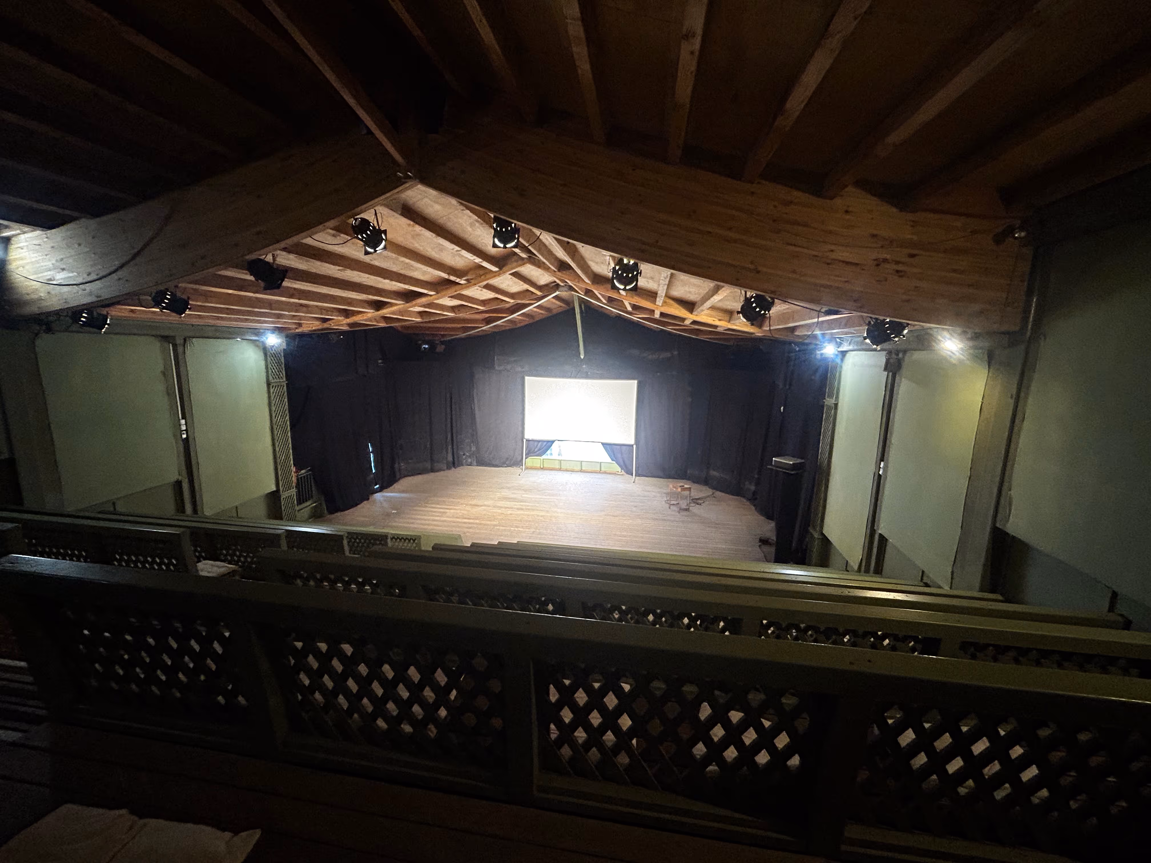 Empty small theater or auditorium with wooden ceiling, stage, and a projection screen.