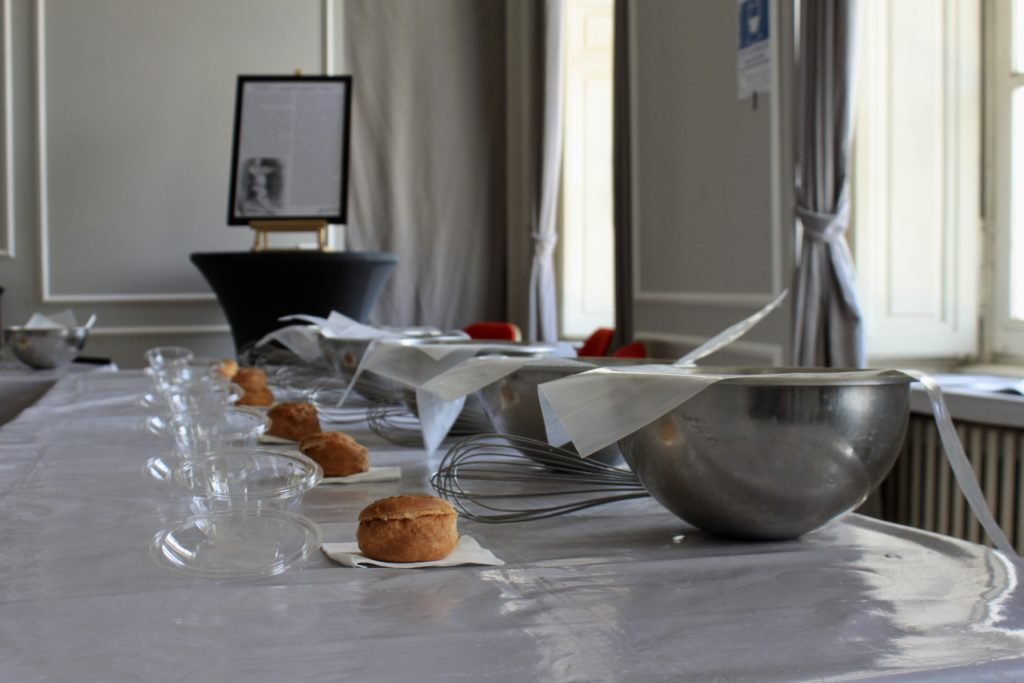 Table set for a baking class with metal mixing bowls, whisks, small glass bowls, and cream puffs on napkins.