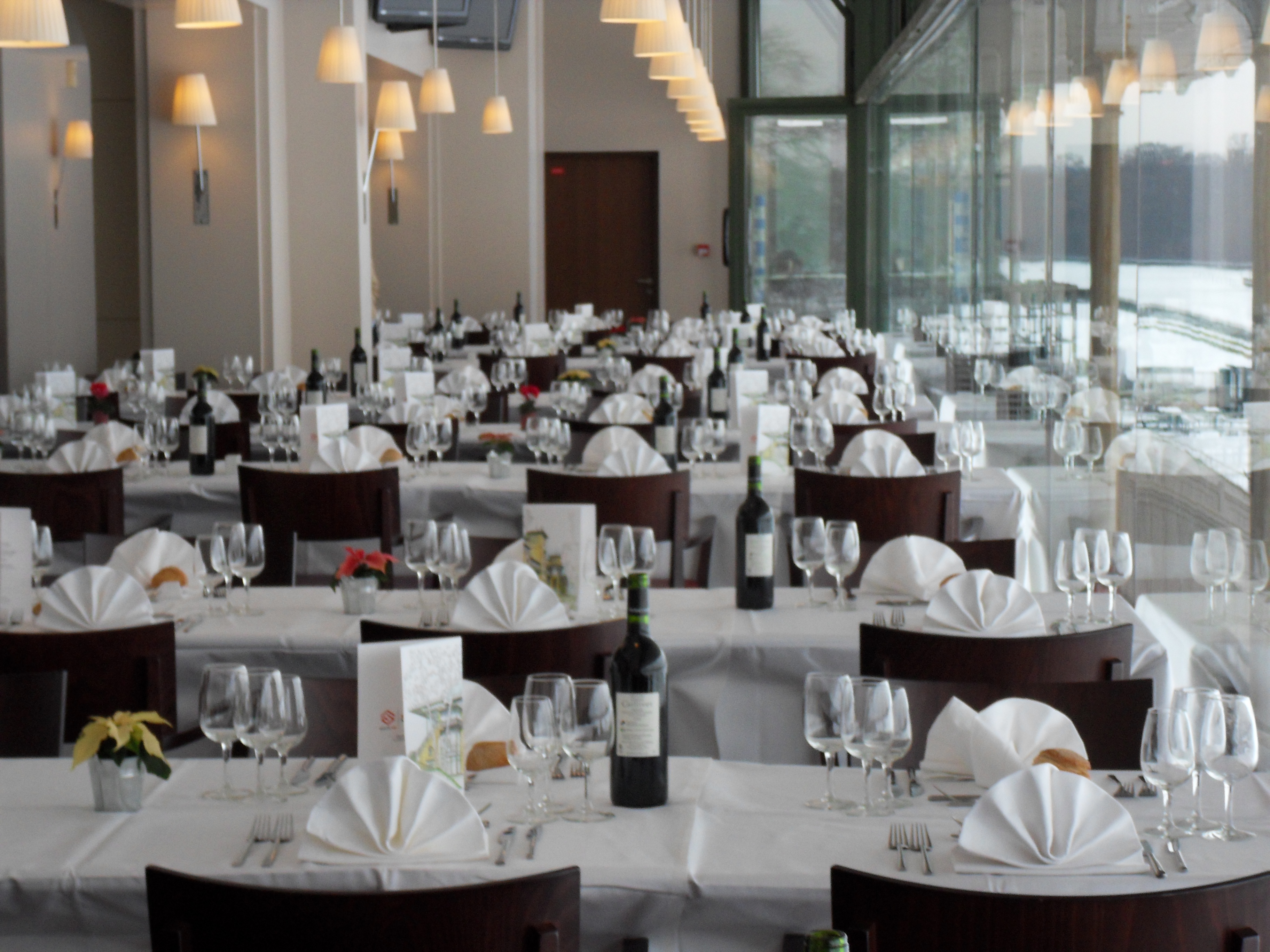 Elegant dining room with multiple tables set with white tablecloths, folded napkins, wine glasses, and wine bottles.
