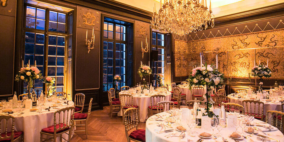 Elegant banquet room with round tables set for dinner, decorated with floral centerpieces and a large chandelier.