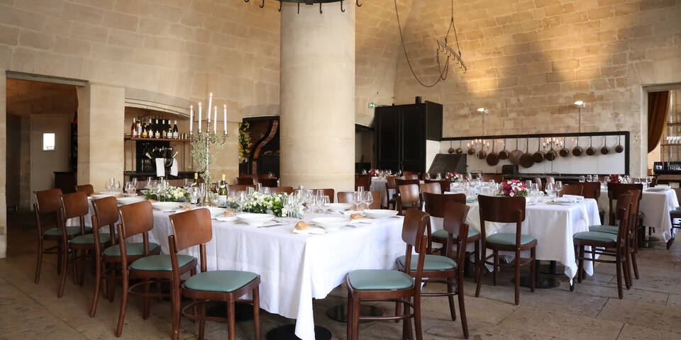Elegant dining room with wooden chairs and tables set with white tablecloths, glassware, and floral centerpieces.