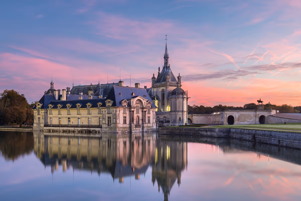 Historic château reflected in the calm water of its moat during a colorful sunset.