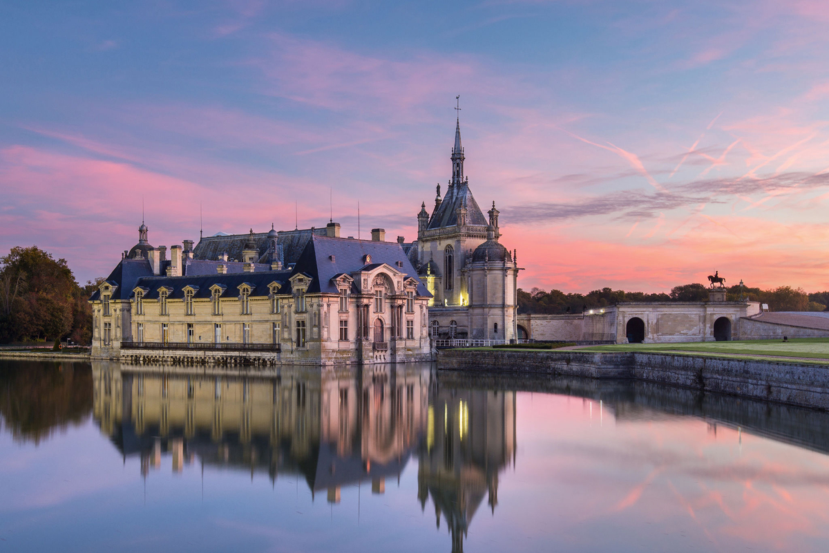 Historic château reflected in the calm water of its moat during a colorful sunset.