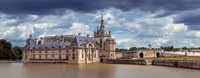 Historic castle with ornate architecture surrounded by moat under a cloudy sky.