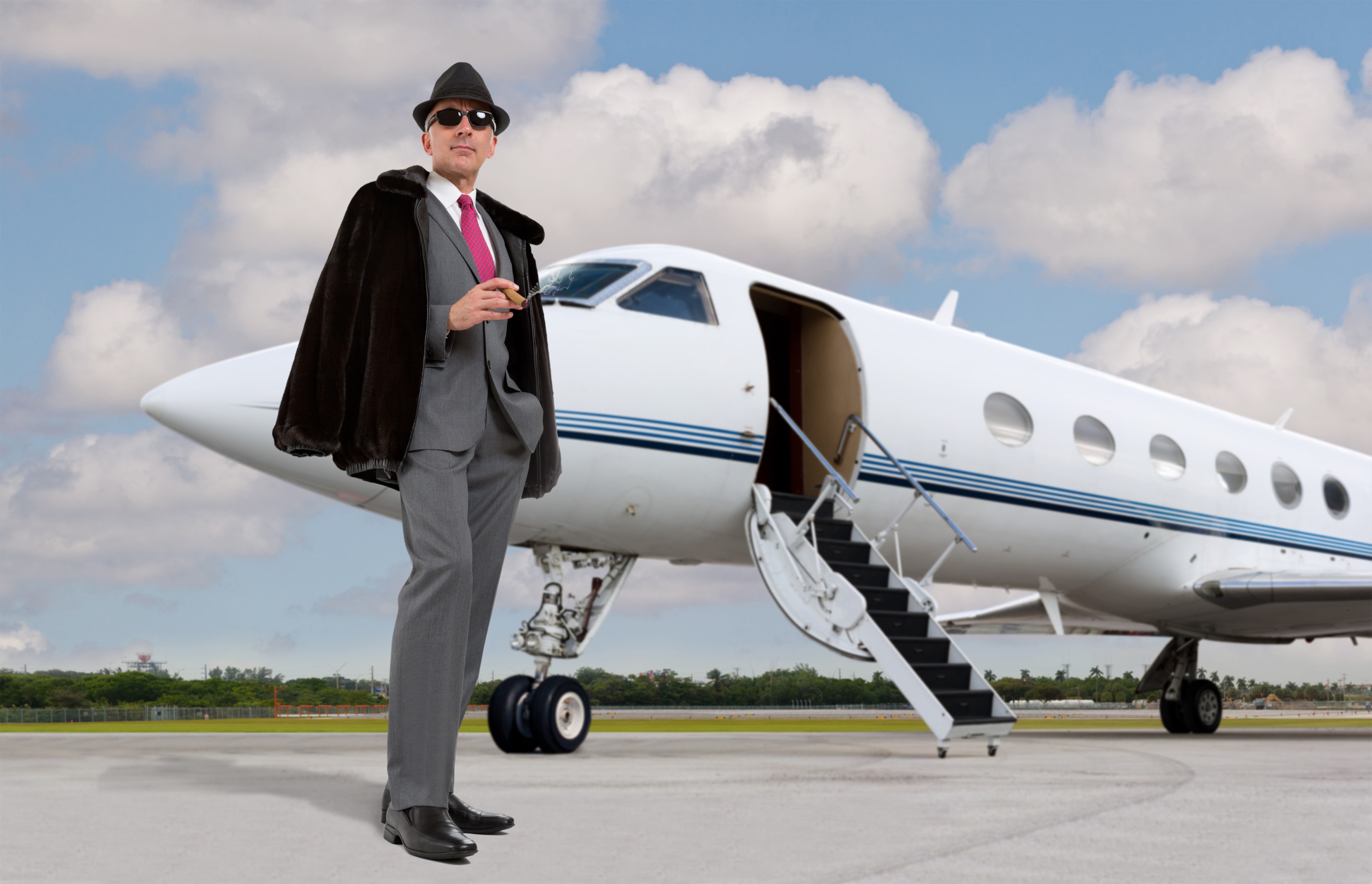 Handsome business man on the steps of a private jet wearing a hat and smoking a cigar
