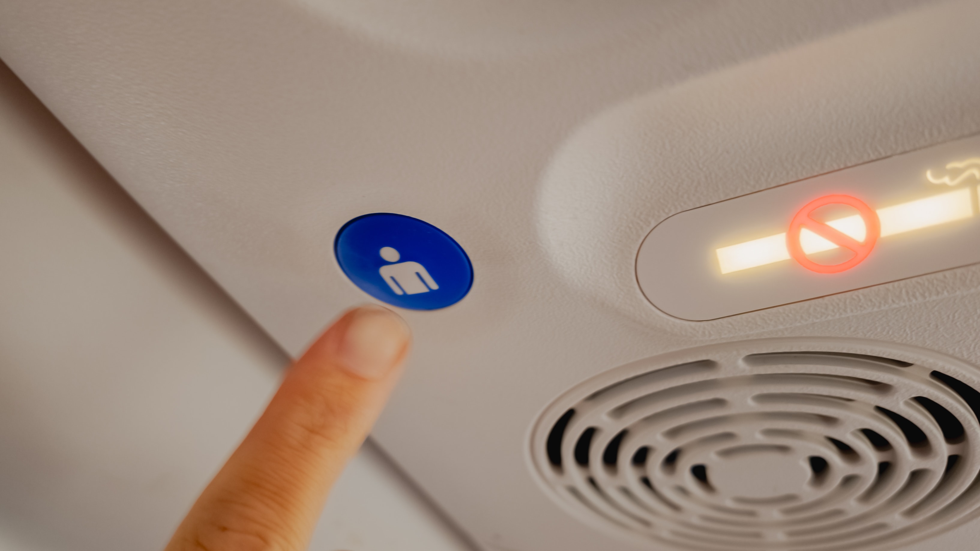 A finger pressing the flight attendant call button next to a no smoking sign inside an airplane cabin, travel safety concept