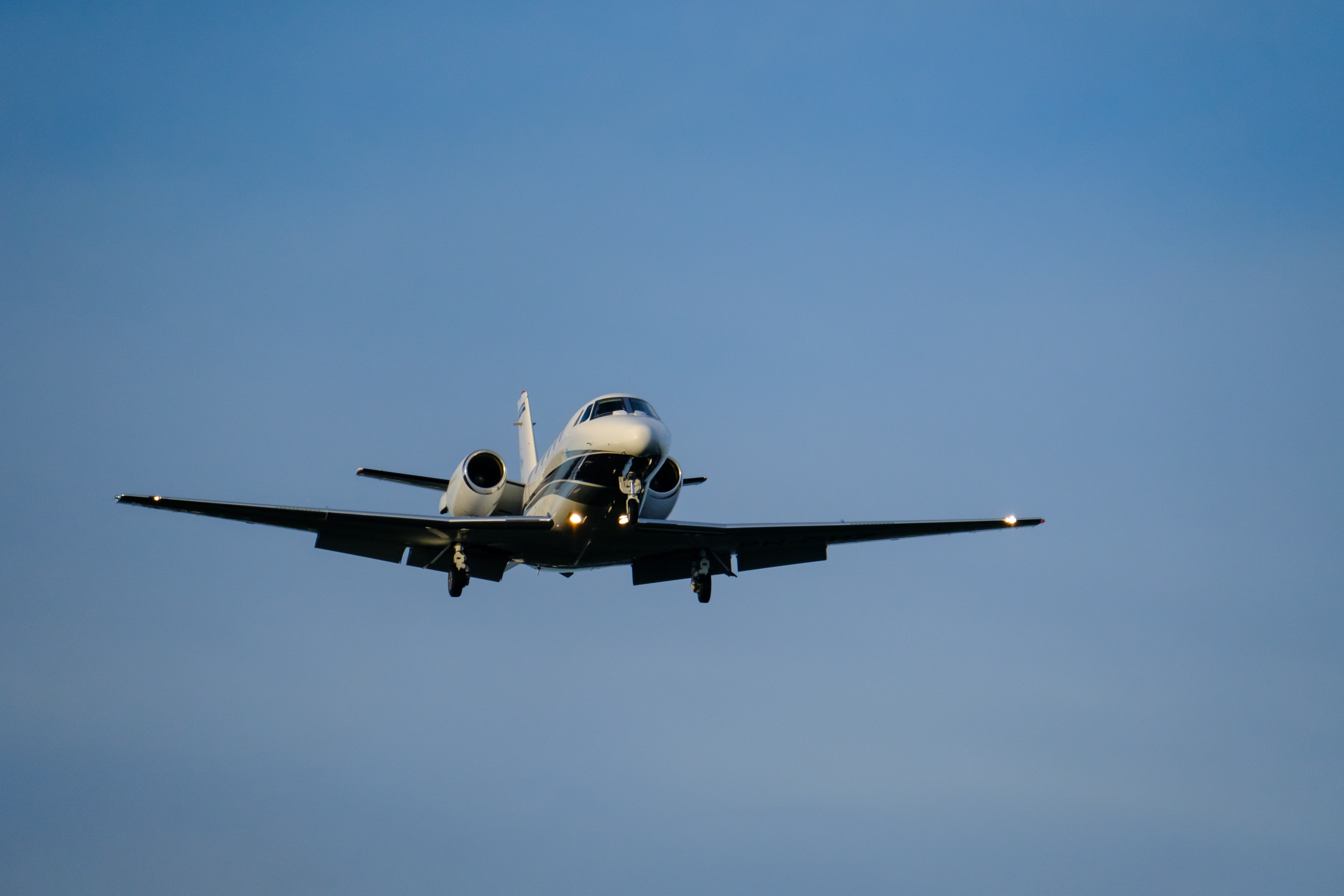 A small business jet approaches the airport with landing lights on.