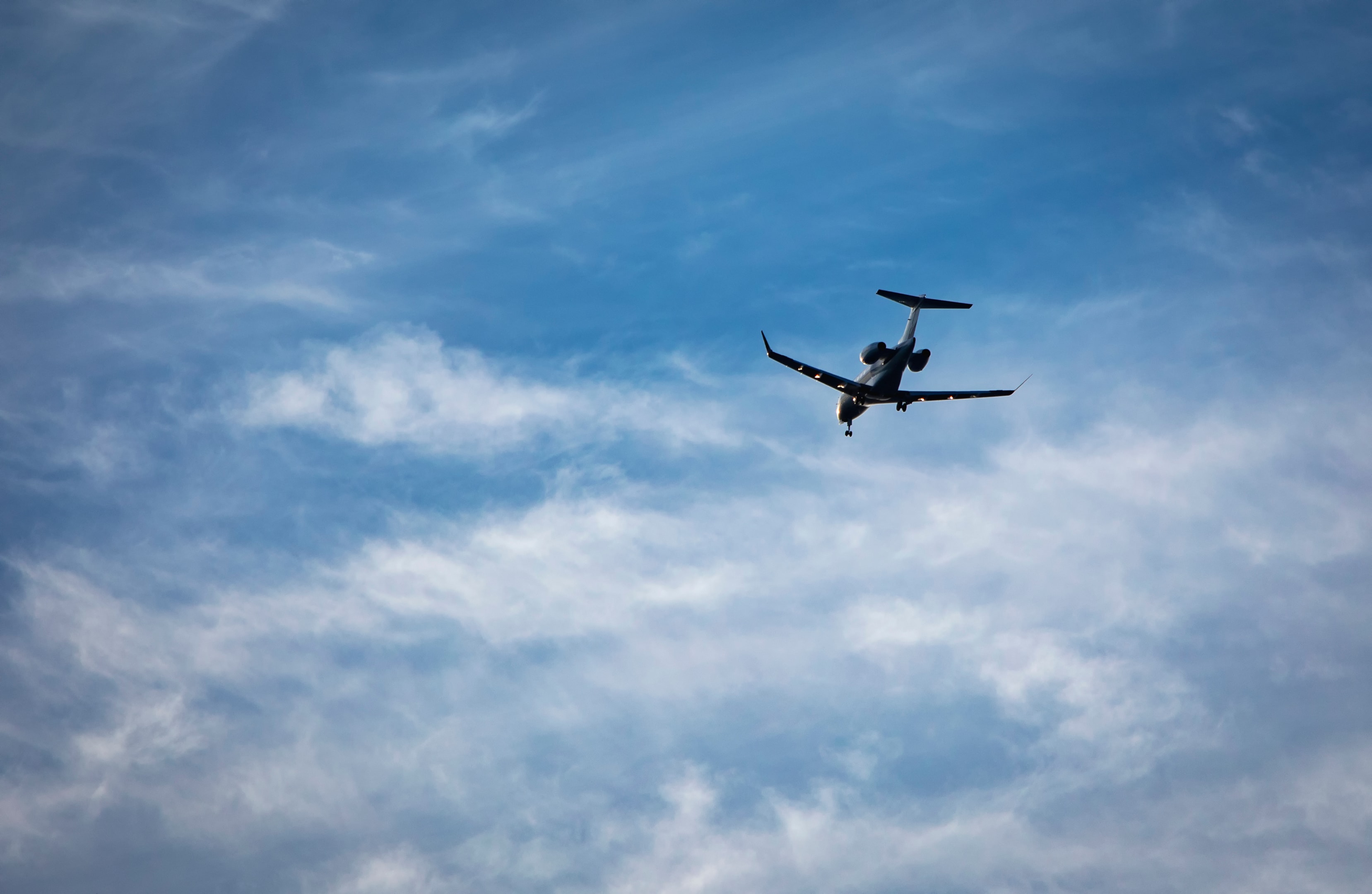 Private jet with landing gear down flying across blue sky with white cirrus clouds. 