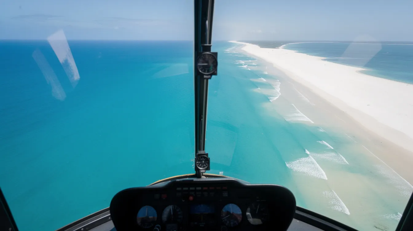 An aerial view from inside a leading edge helicopter showcases the stunning turquoise ocean water contrasting with a pristine white sandy coastline, perfect for those seeking a lifetime experience through helicopter tours.