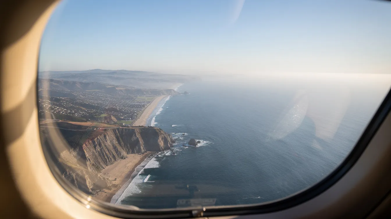 The image depicts a breathtaking view from a small jet window, showcasing the stunning California coastline with the deep blue Pacific Ocean below. This scene captures the essence of private jet travel, highlighting the beauty of flying privately along the West Coast.
