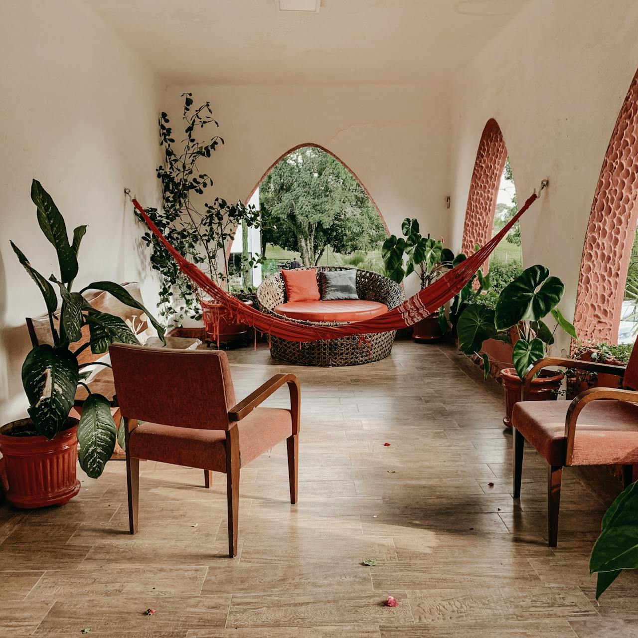 A room with a hammock, chairs, and potted plants.