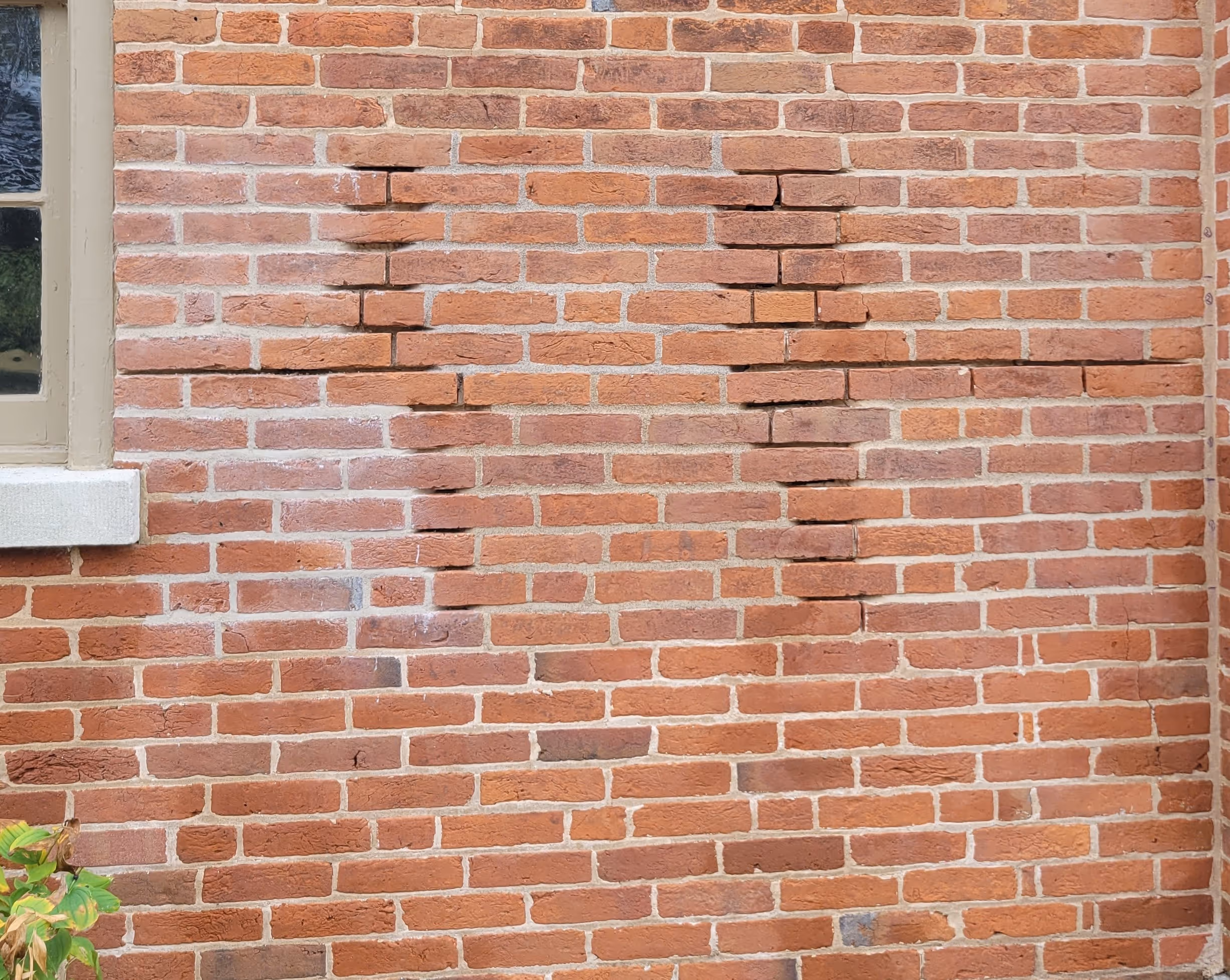 Red brick wall with visible repair area where bricks are discolored and mortar lines disrupted.