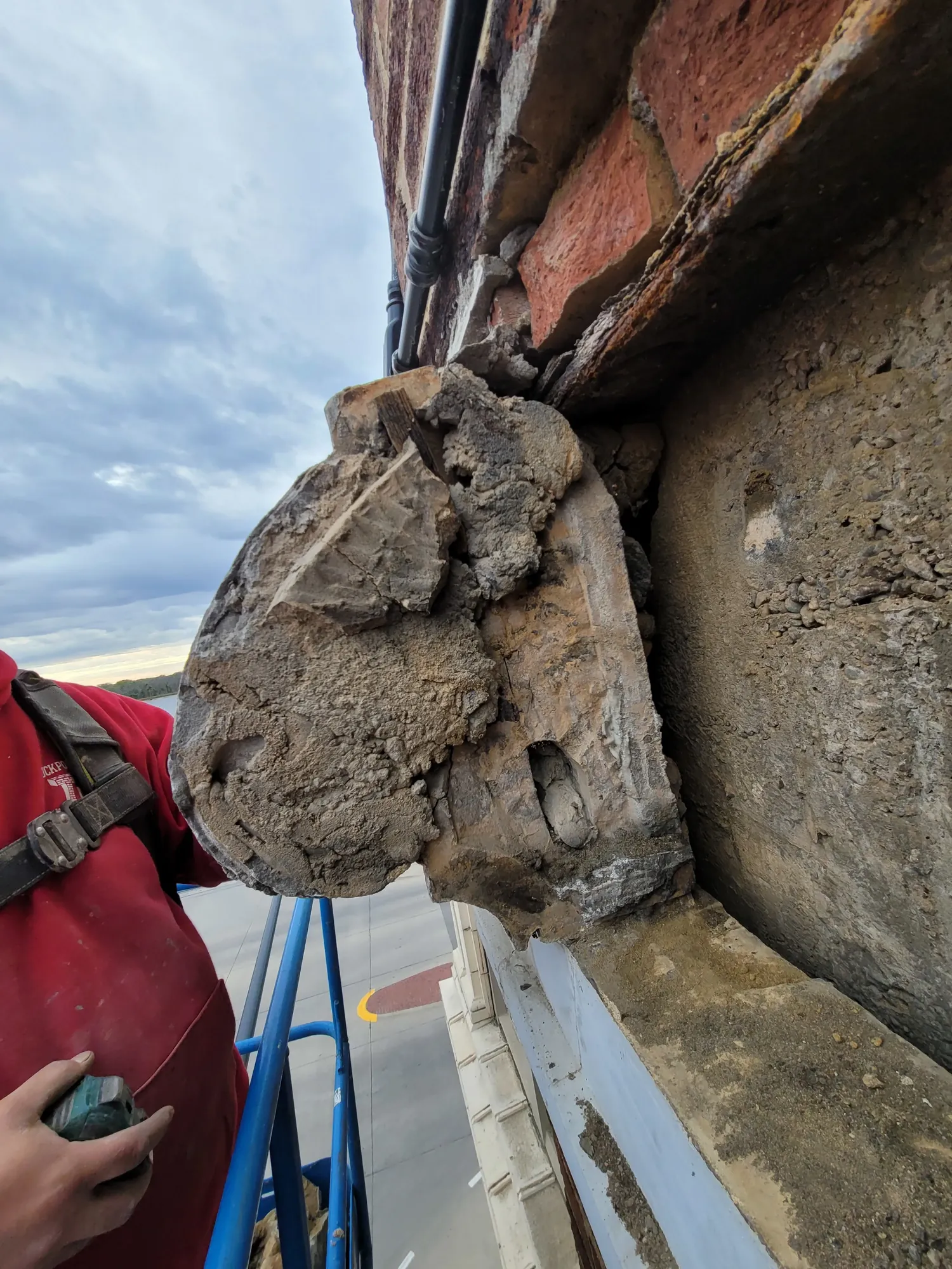 Close-up of a person's hand holding a power tool repairing a damaged brick building corner with crumbling concrete.
