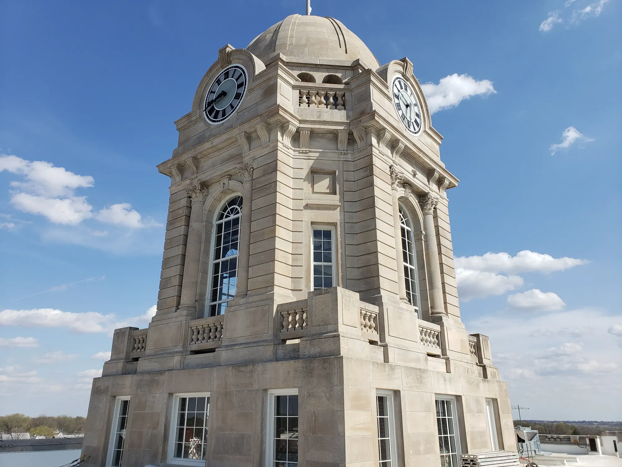 Stone clock tower with two visible clock faces showing 3:45 under a blue sky with scattered clouds.