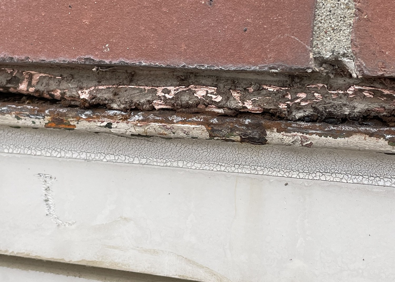 Severely corroded steel lintel above a window head showing visible voids and active rust jacking on a commercial school building