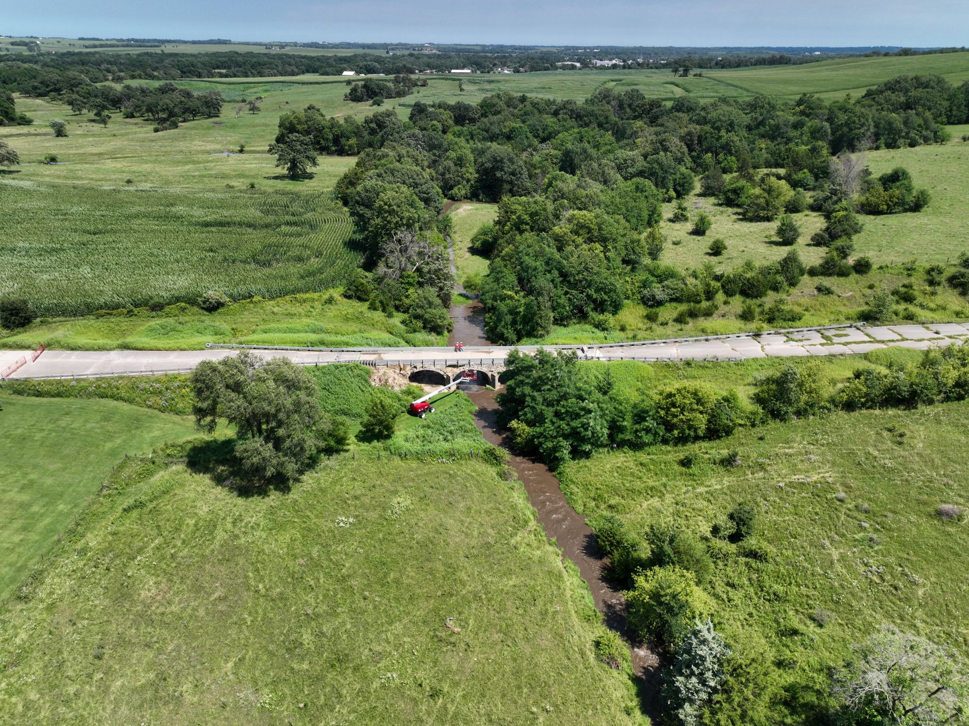 Ely's Stone Bridge in its Jones County farmland setting, aerial lift on site during the July 2026 assessment.