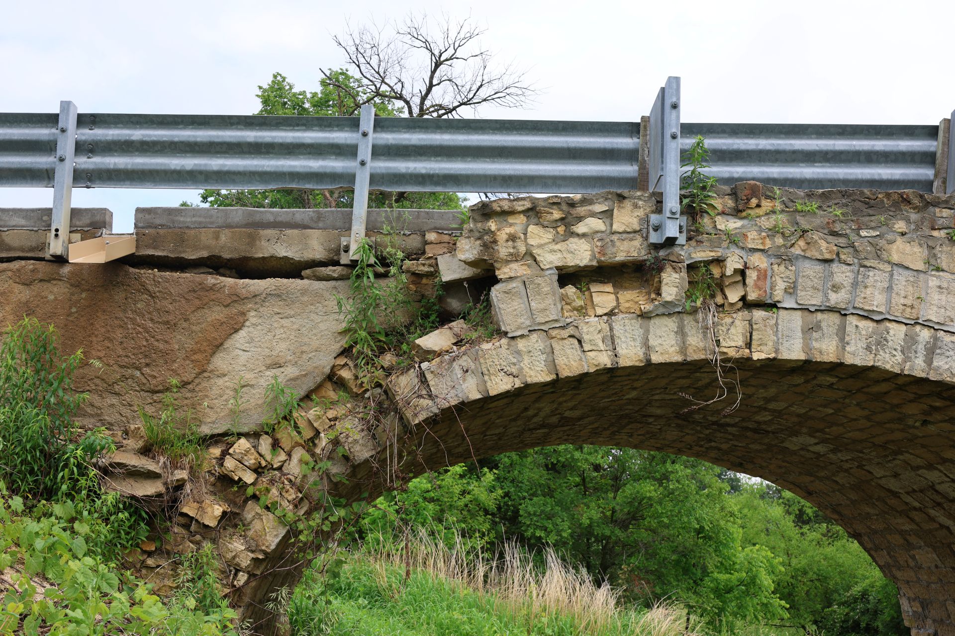 Guardrail and concrete deck edge spanning open air where the spandrel wall beneath has collapsed.