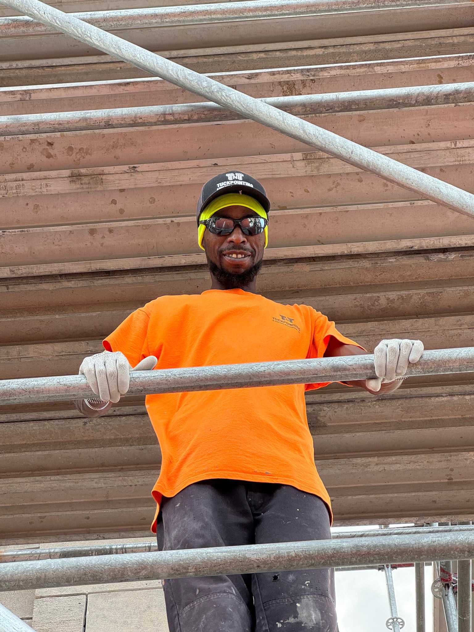 Thomas Collins, TNT Tuckpointing tuckpointer, standing on scaffolding in a TNT shirt and cap