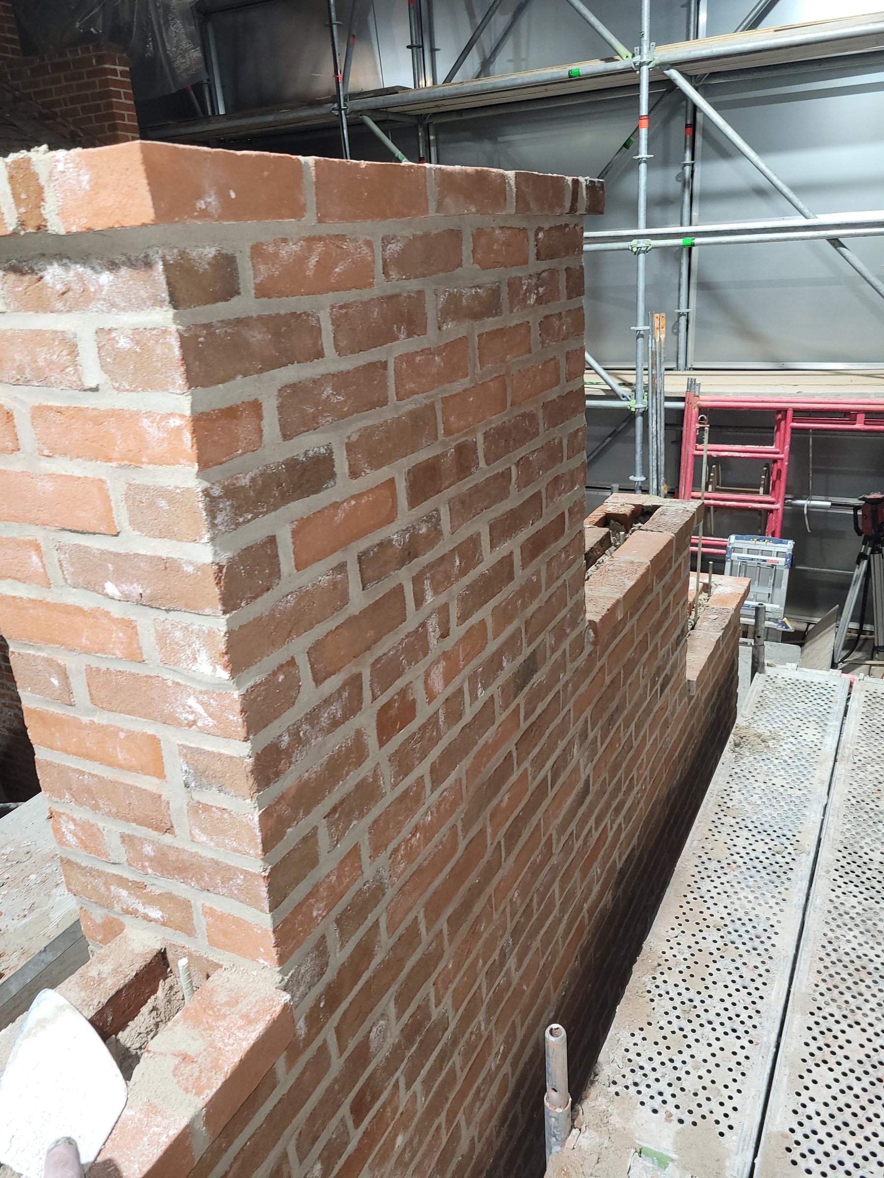Rebuilt wing corner at full height beside the scaffold walkway, custom brick laid to match the original