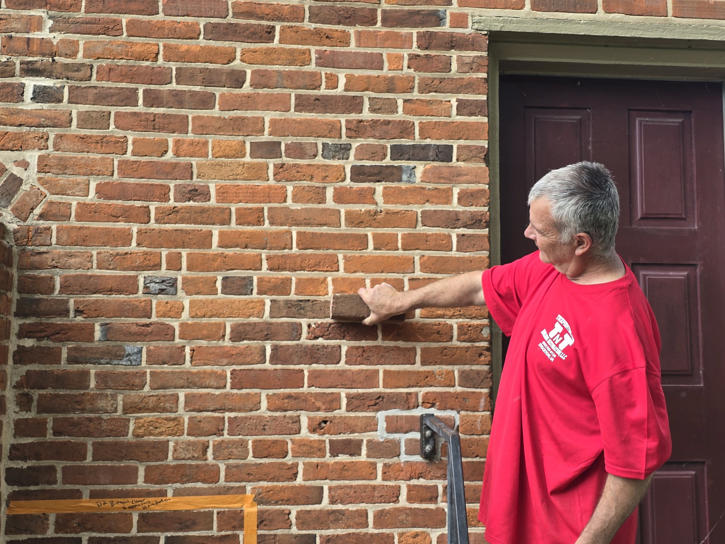 Mason holding a sample brick against the original 1840s brick wall to check size and color