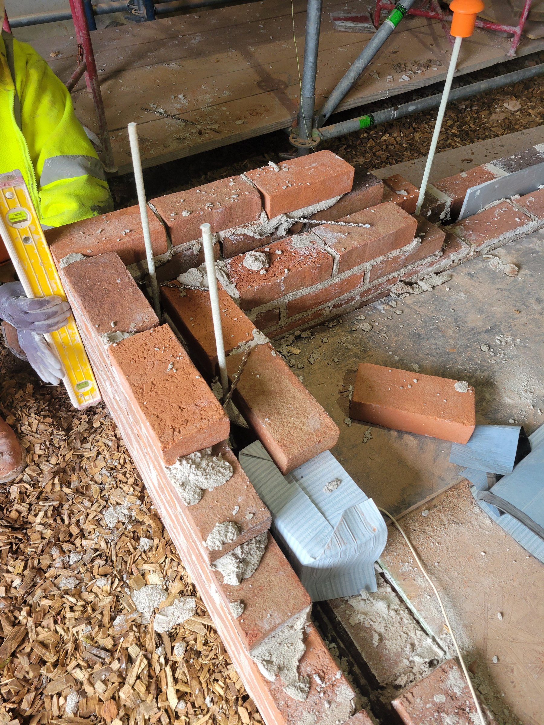 Mason laying custom brick at a rebuilt wing corner, checking it with a level as the wall rises