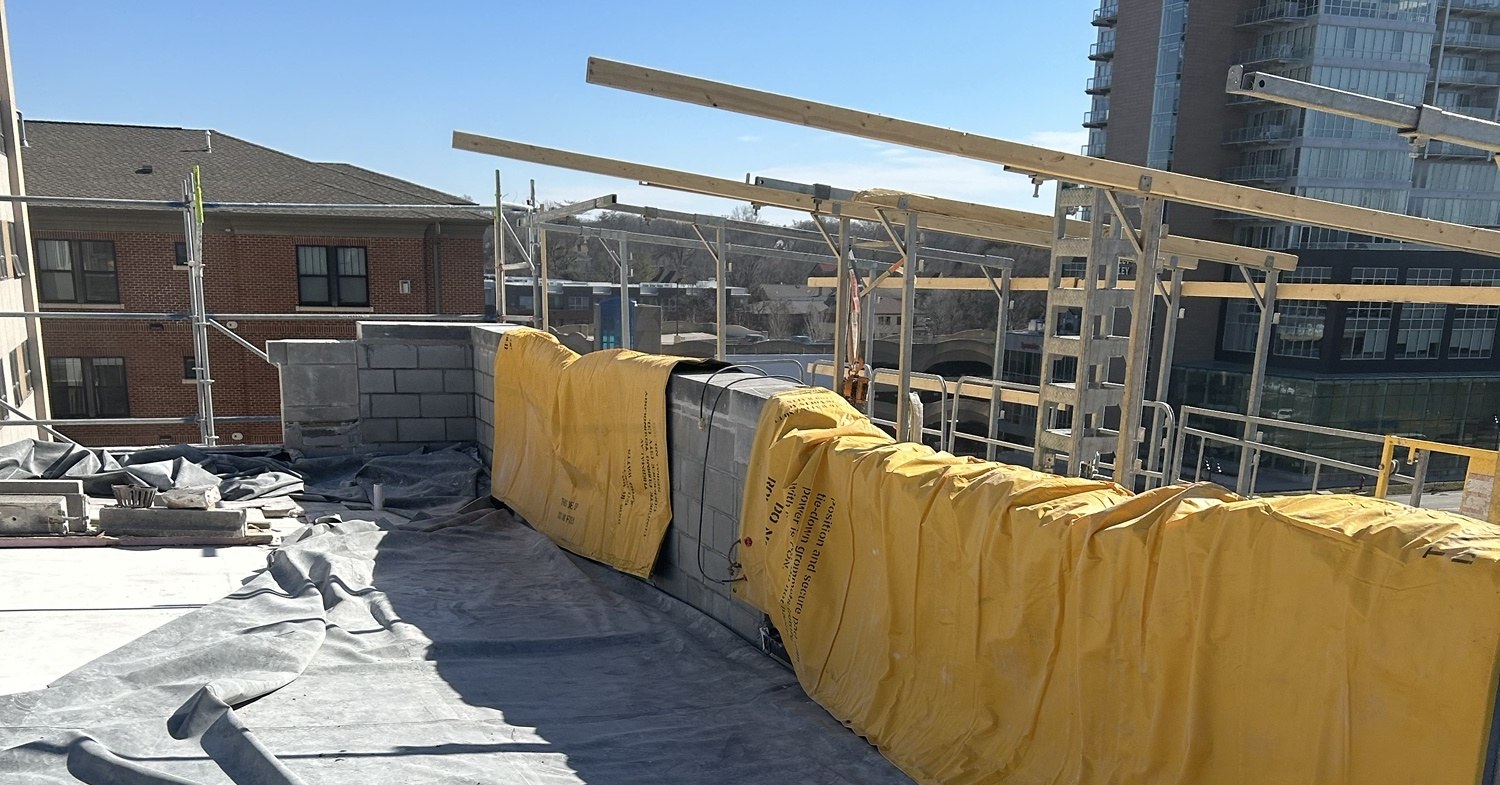 Yellow heated curing blankets covering a rebuilt masonry parapet on a downtown Iowa City rooftop in February, with scaffold and temporary roofing around the work