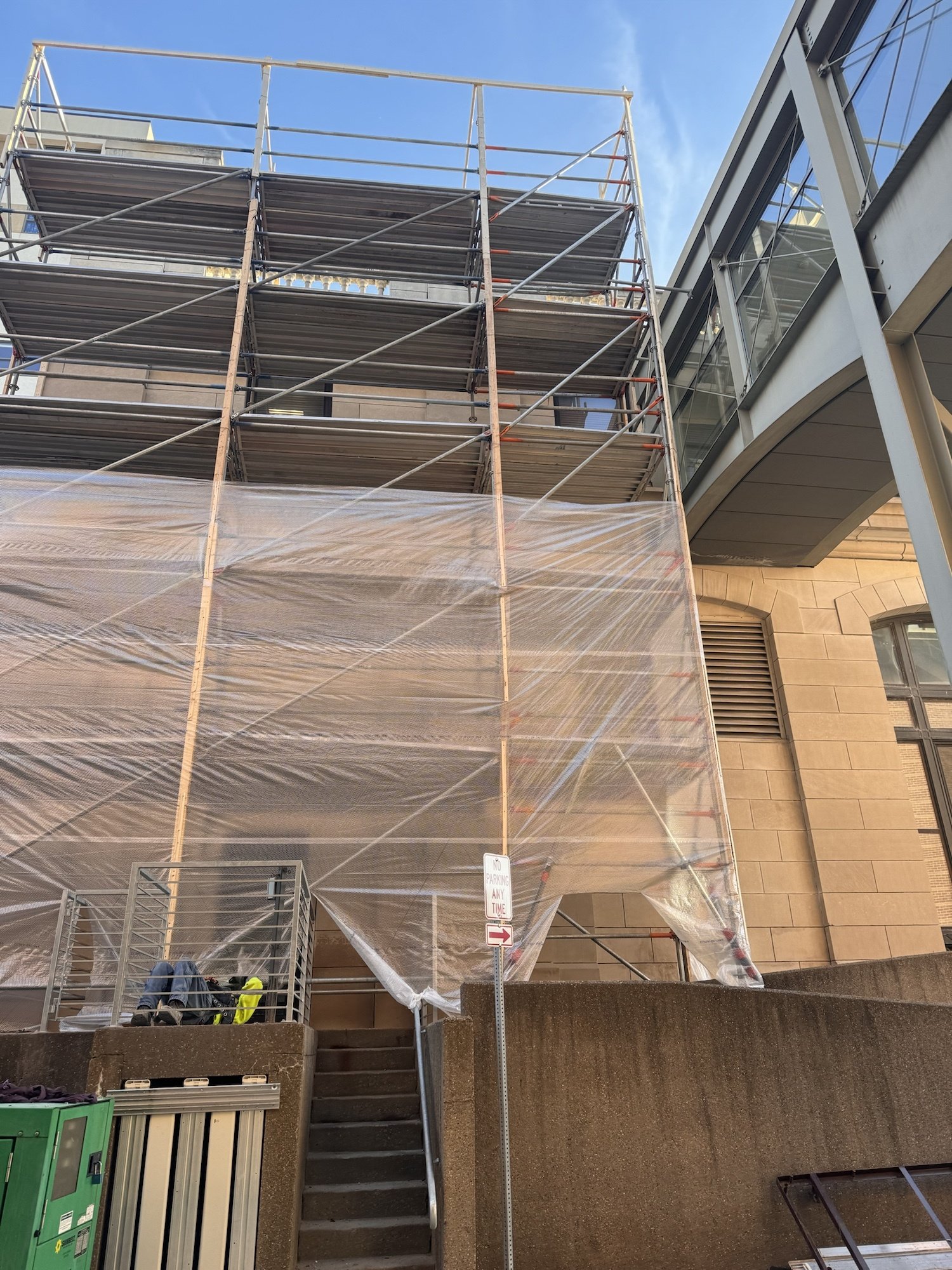 System scaffold wrapped in clear poly sheeting to form a winter enclosure against a limestone building in downtown Iowa City