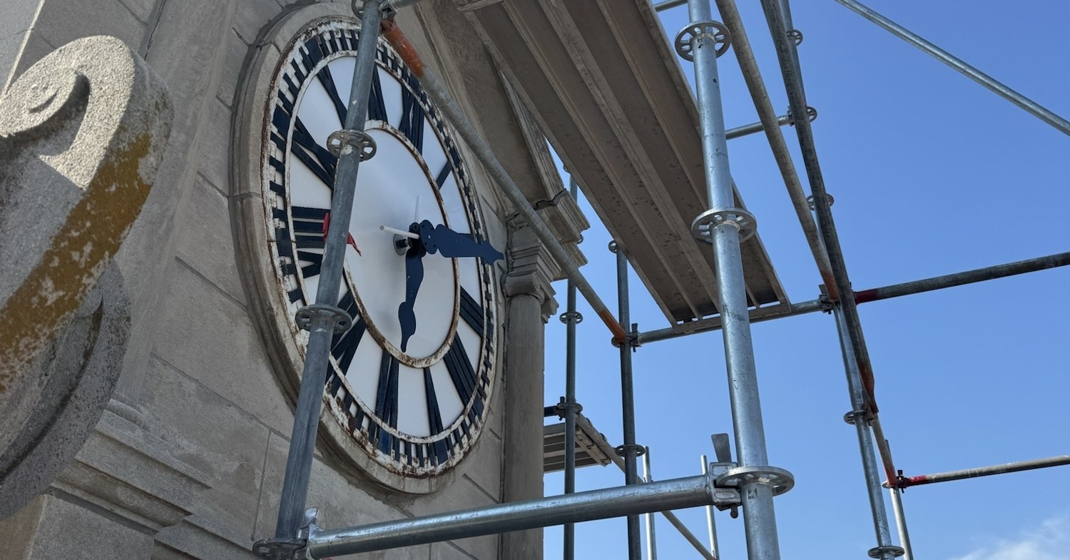 Clock face on a historic limestone courthouse tower in Iowa, seen through scaffolding during masonry restoration in September 2026