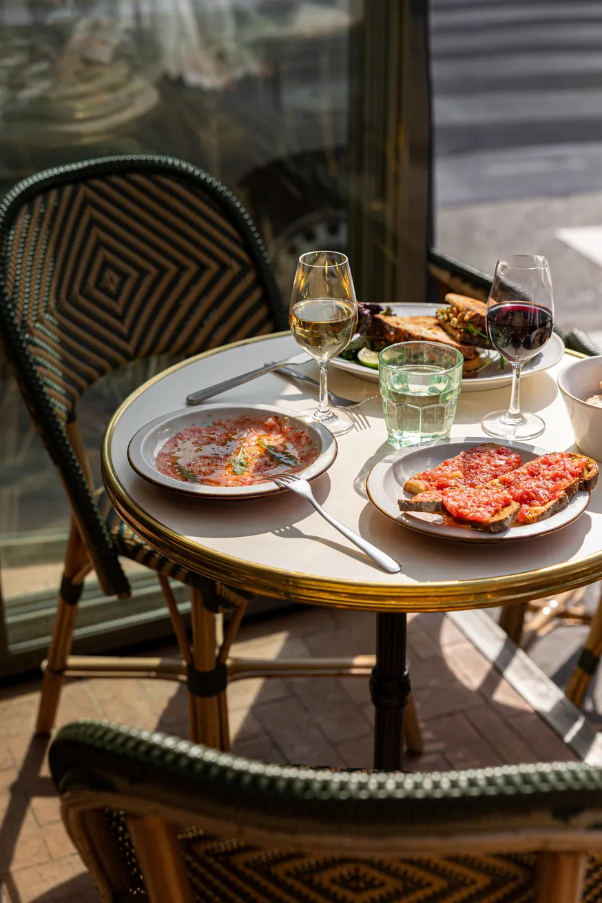Table de café en terrasse avec deux verres de vin, assiettes de plats italiens et chaises tressées.