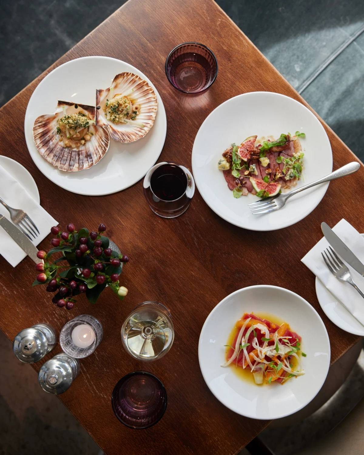 Overhead photograph of plated dishes, including scallops in their shells, on a restaurant table