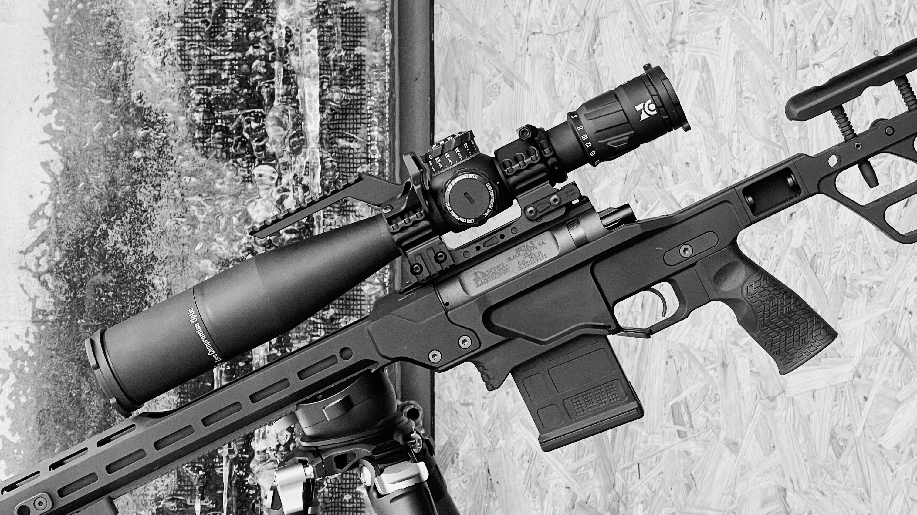 Black precision rifle with scope mounted on bipod against textured background.