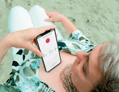 A woman laying on a beach holding a cell phone.
