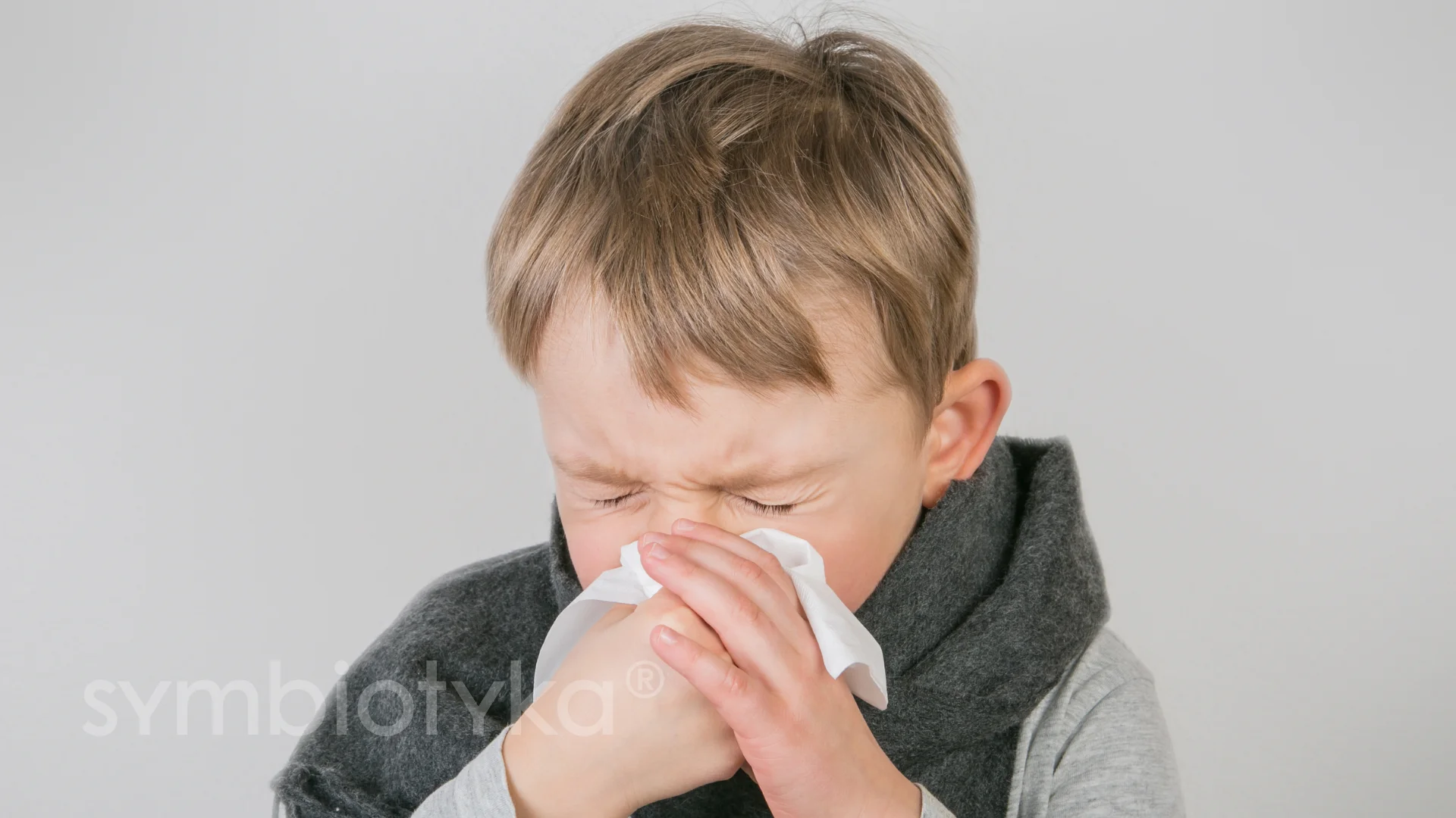 A young boy is blowing his nose with a tissue.