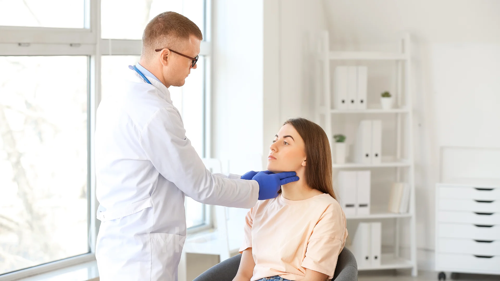 A doctor examines a patient's ear in an office.