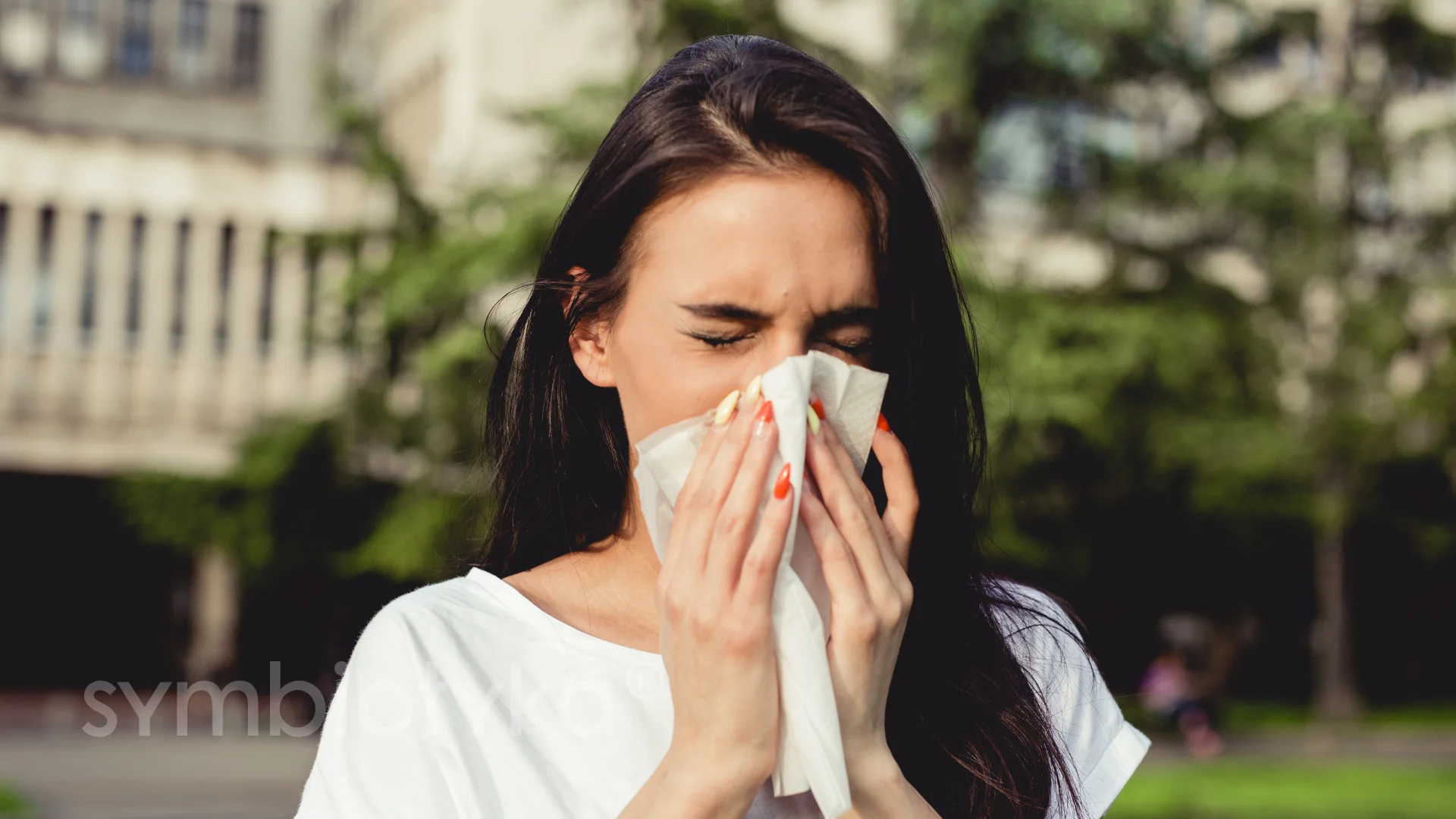A woman is blowing her nose outside.
